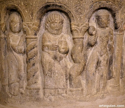 Personajes bajo arcos con columnas labrados en la pila bautismal
